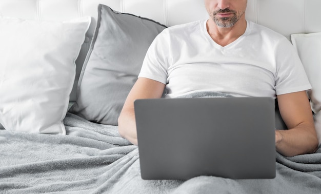 Drukke volwassen man aan het werk op laptop in bed