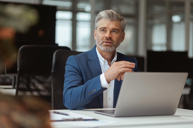 Drukke volwassen zakenman die op laptop werkt terwijl hij in moderne coworking zit