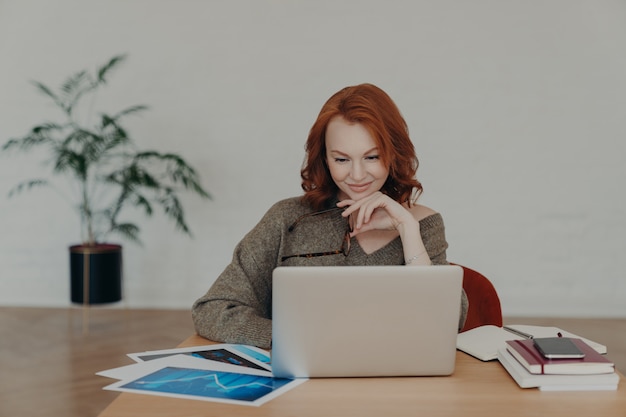 Drukke vrouw freelancer houdt bril voor zichtcorrectie, poseert thuis desktop