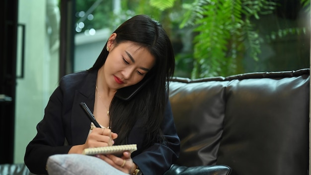 Drukke vrouwelijke financieel adviseur die een telefoongesprek voert en aantekeningen maakt op een notebook