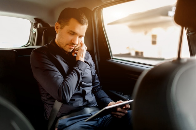 Drukke zakenman in een taxi. Multitasking-concept. Passagier rijdt op de achterbank en werkt tegelijkertijd. Spreekt op smartphone en gebruikt tablet-pc.
