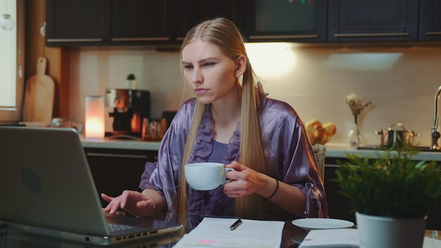 Drukke zakenvrouw in huis badjas drinken van een kopje koffie.