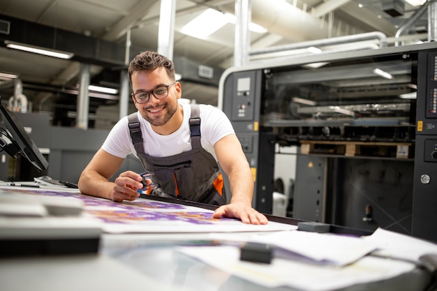 Drukkerijmedewerker die de kwaliteit van het afdrukproces controleert en de kleuren controleert met een vergrootglas.