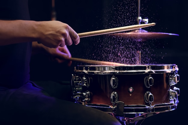 Drum sticks hitting snare drum with splashing water on black background under studio lighting close up.