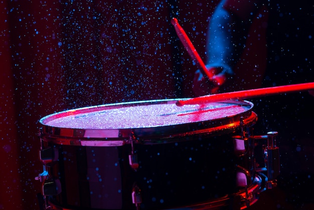 Drum sticks hitting snare drum with splashing water on dark background