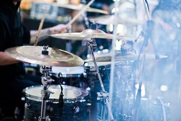 Drummer play at drum set on stage in a concert hall behing glass wall