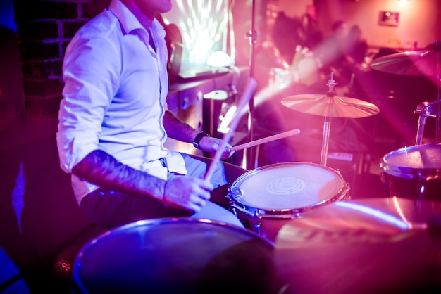 Drummer playing on drum set on stage. Warning - Focus on the drum, authentic shooting with high iso in challenging lighting conditions. A little bit grain and blurred motion effects.