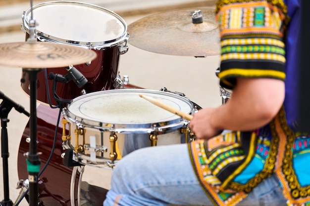 Drummer playing musical percussion instrument drums with sticks, musical concept with working drum set on concert stage. Drumsticks and drums, male hands playing drum kit outdoor, close up