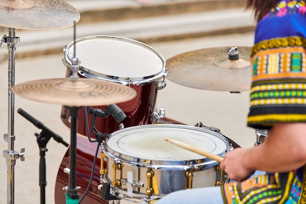 Drummer playing musical percussion instrument drums with sticks, musical concept with working drum set on concert stage. Drumsticks and drums, male hands playing drum kit outdoor, close up