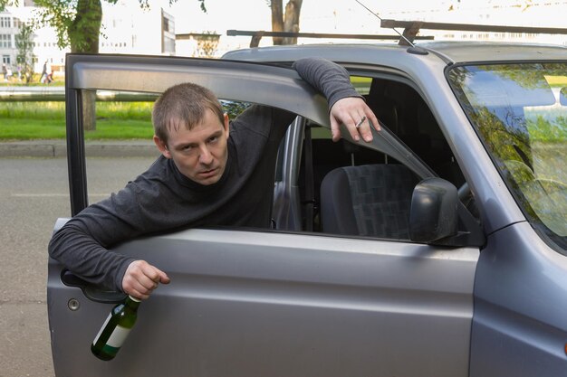 Photo drunk driver with a bottle of alcohol holding on to the door of his own car