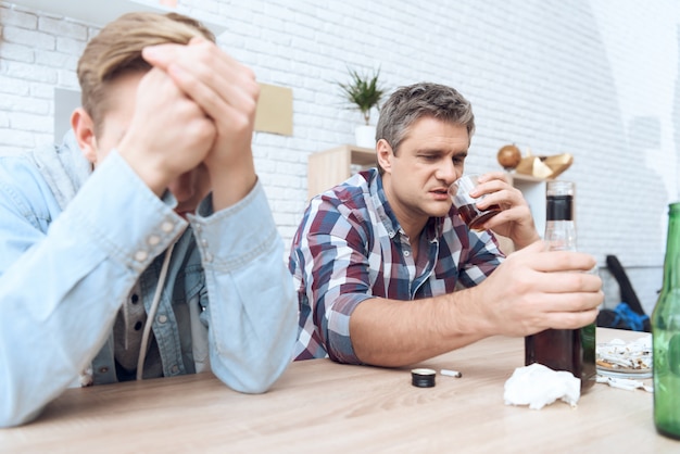 Drunk father is sitting at table with glass.