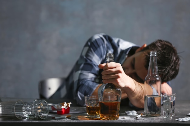 Foto uomo ubriaco seduto a tavola con alcol e droghe concetto di alcolismo