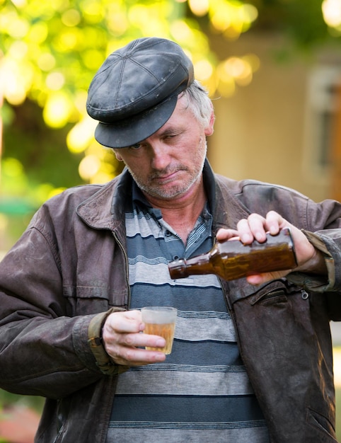 Drunk man with bottle of beer and glass on natural background