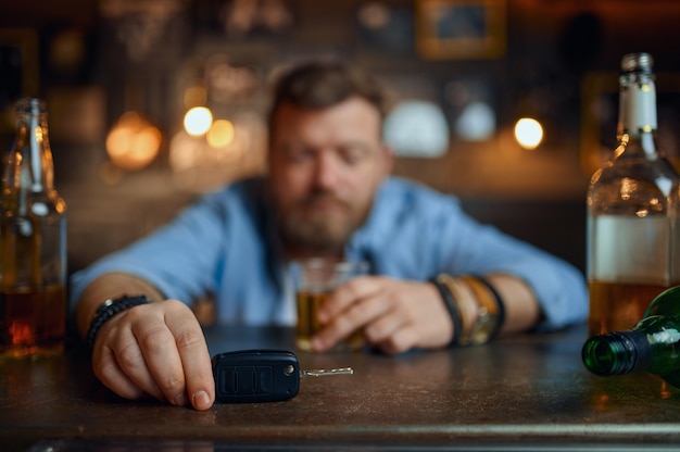 Пьяный мужчина с ключом от машины сидит за стойкой в баре