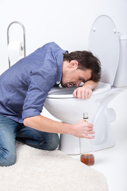 Drunk man with wine bottle in toilet.