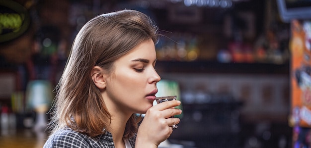 Donna ubriaca con in mano un bicchiere di whisky o rum. donna in depressione. giovane bella donna che beve alcolici. bicchiere da whisky scozzese isolato al bar o al pub in abuso di alcol e concetto alcolico