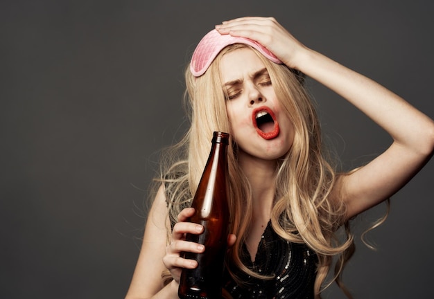 Drunk woman with a bottle of beer bright makeup blonde pink mask for sleep