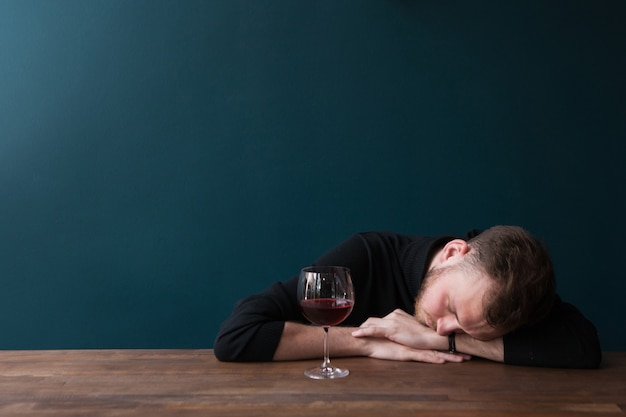 Пьяный молодой мужчина спит в баре. Неудачное свидание. Проблемы у взрослых иф, усталый мужчина с красным вином на синем фоне со свободным пространством. Плохой день, проблемы в бизнес-концепции
