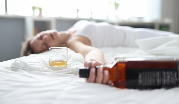 Drunk young woman lies in bed in bottle of alcohol