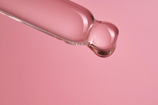 Druppel met serum of cosmetische olie op een roze achtergrond