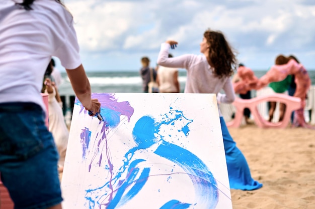 Druppel schilderen openluchtkunstuitvoering met dansende meisjes op zandstrand aan zee Schilderkunstenaar tekenen op wit canvas abstracte afbeelding in druppelen schilderen abstracte kunsttechniek Creatief kunstfestival