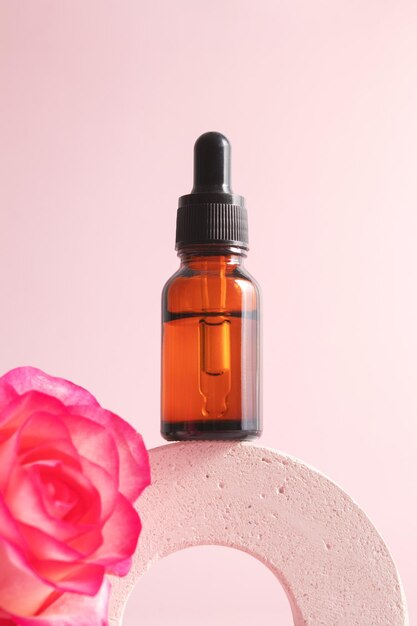 Druppelflesje met serum op een podium op roze achtergrond met roos