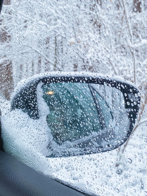 Druppels op de zijruit van de auto waardoor je het winterlandschap kunt zien