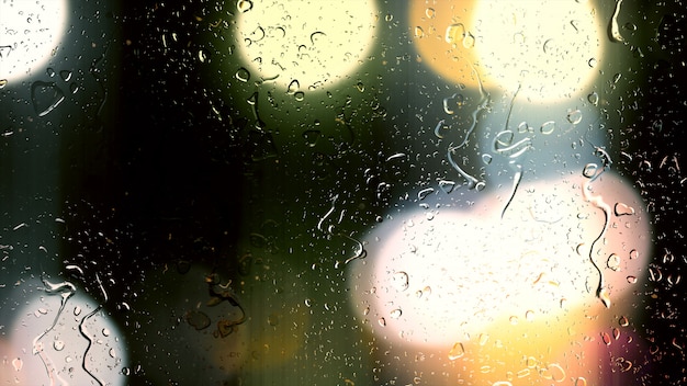 Druppels regen stromen langs het glas tegen de bokehachtergrond van rijdende auto's