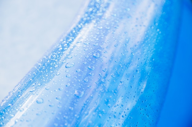 druppels water - op het blauwe oppervlak van een opblaasbaar speelgoedwiel. Opblaasbaar strandmatras met waterdruppels op een zonnige dag. Helder blauw kinderbadoppervlak met waterdruppels erop. Zomer zwembad