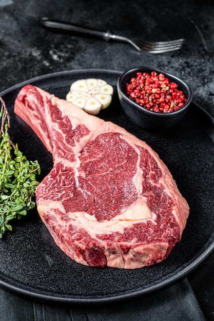 Dry aged cowboy or rib eye steak raw beef meat with herbs Black background Top view