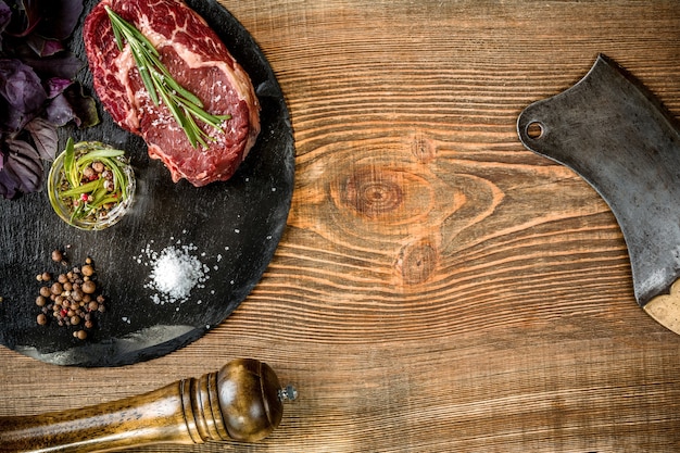Dry aged raw beef steak with ingredients for grilling on wooden background. Top view. Copy space. Still life. Flat lay