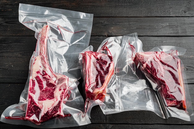 Bistecca invecchiata a secco sottovuoto prodotti a base di carne in confezione di plastica set tomahawk t bone e tagli di bistecca club su sfondo nero del tavolo di legno