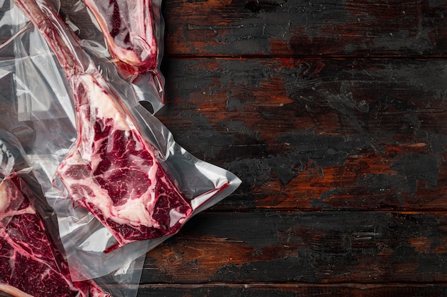 Dry aged steak in a vacuum. Meat products in plastic pack set, tomahawk, t bone and club steak cuts, on old dark wooden table, top view flat lay