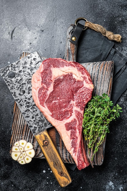 Dry aged tomahawk rib eye steak raw beef meat on butcher table\
black background top view