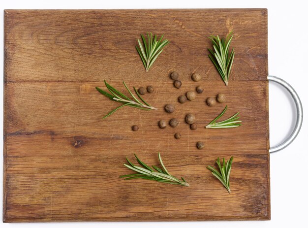 Dry allspice peas and rosemary branches on a wooden background