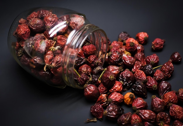 Dry berries of red rosehip in a glass jar laid out on a black background closeup