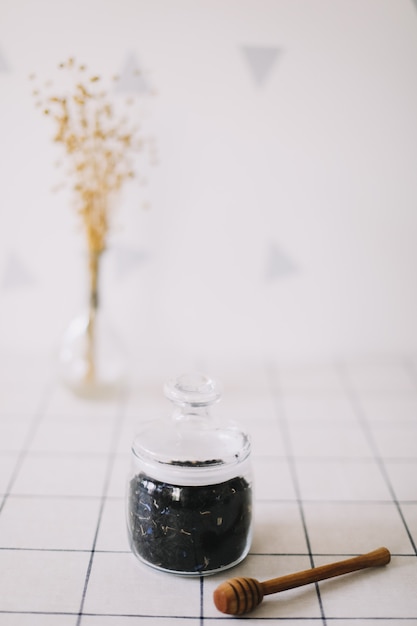 Dry black tea in glass jar and honey spindle on kitchen background