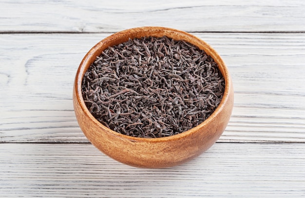 Dry black tea in wooden bowl on white wooden background