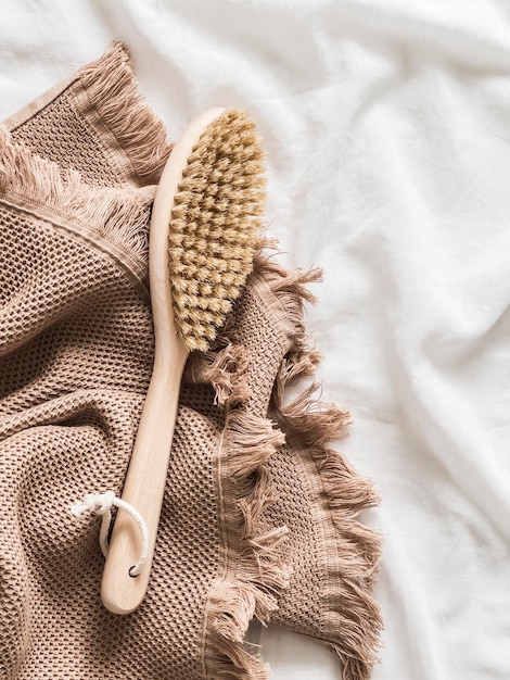 A dry body massage brush with natural bristles and a beige cotton towel on a white background top view