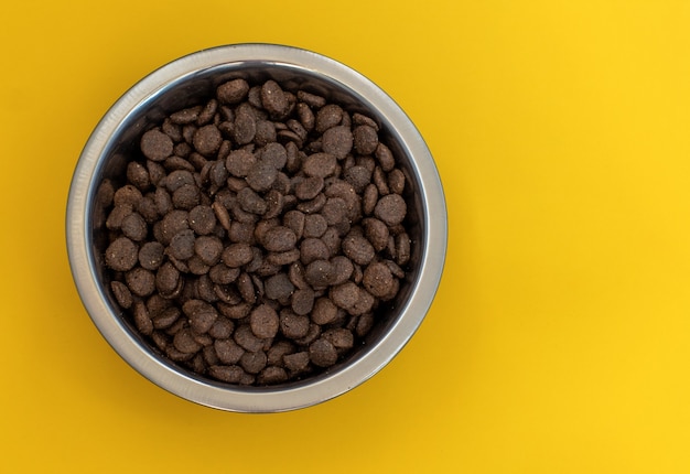 Dry brown pet food for cats or dogs in a metal bowl on a yellow