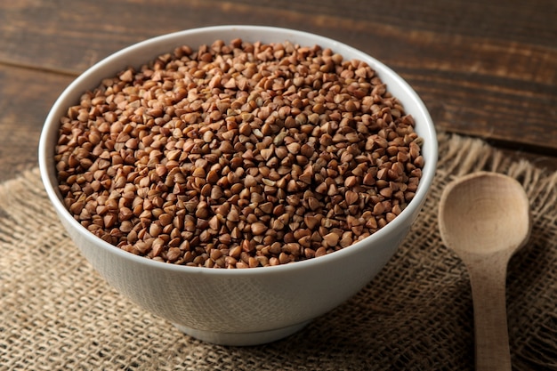 Dry buckwheat groats in a white bowl with a spoon on a wooden brown table. cereals. healthy food. porridge.