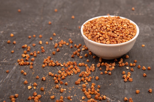 Dry buckwheat in a white ceramic bowl on a black textured table