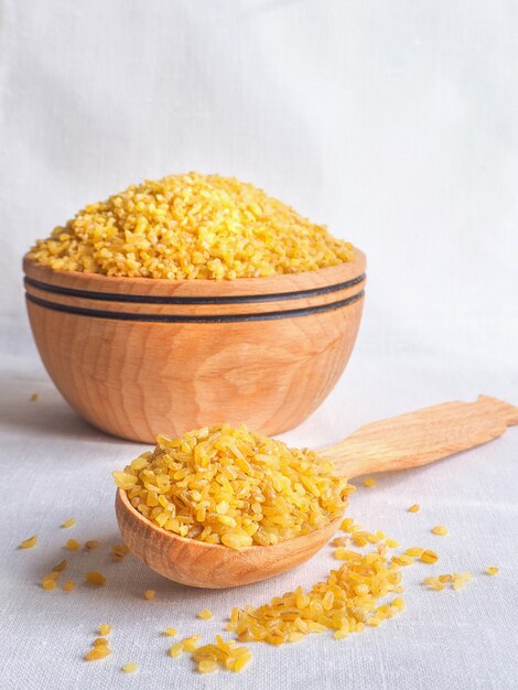 Dry bulgur wheat in wooden bowl. Spilled bulgur.