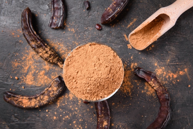 Dry carob pods and carob powder over dark background