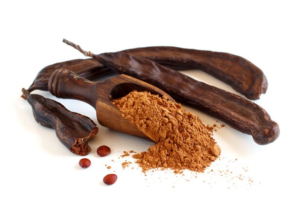 Dry carob powder in a scoop and pods close up isolated on white