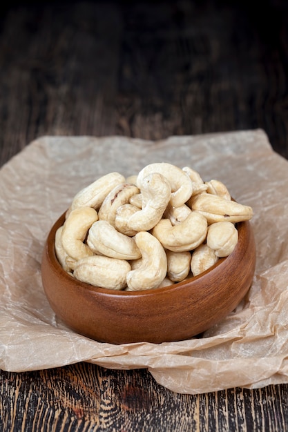 Dry cashew nuts on an old wooden table and in a wooden bowl, a pile of cashew nuts on the table and in a wooden plate while eating