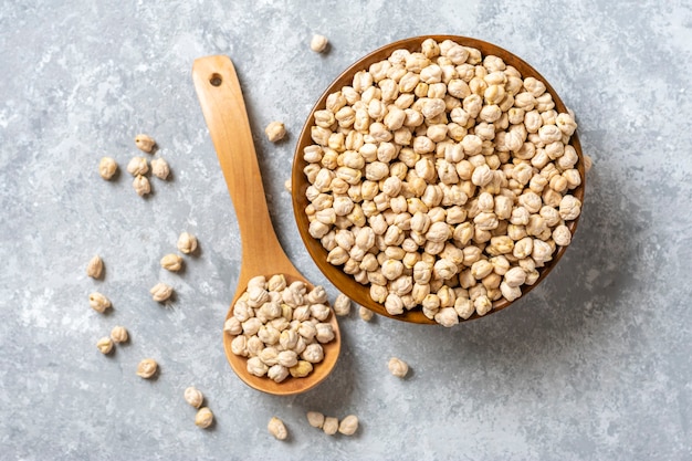 Dry chickpeas in wooden bowl with wooden spoon on concrete background
