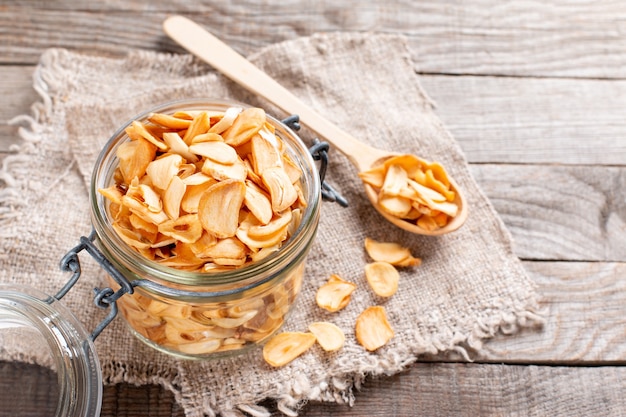 Dry chopped garlic slices in a glass jar on a wooden table, empty space for text