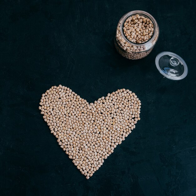 Dry clean chickpeas in glass jar. Heart made of organic uncooked garbanzo. Black background. Plant based protein. Beans for making healthy dish