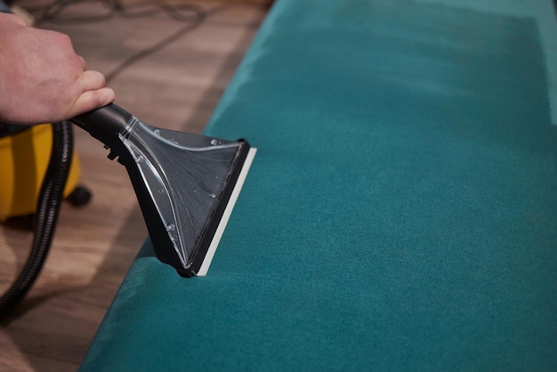 Работник химчистки удаляет грязь с дивана в помещении